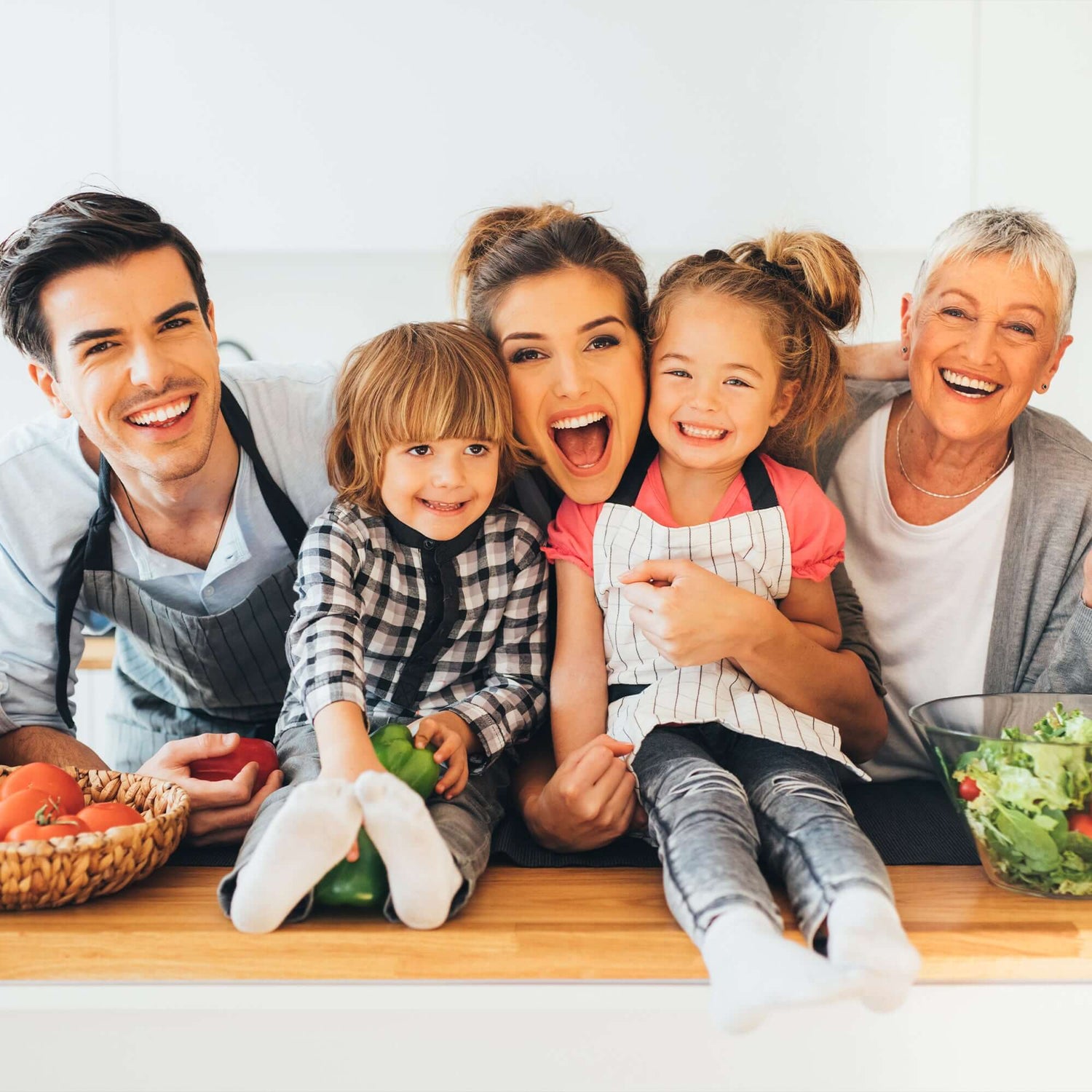 Happy family cooking together in the kitchen, embracing and smiling around fresh vegetables on the counter.