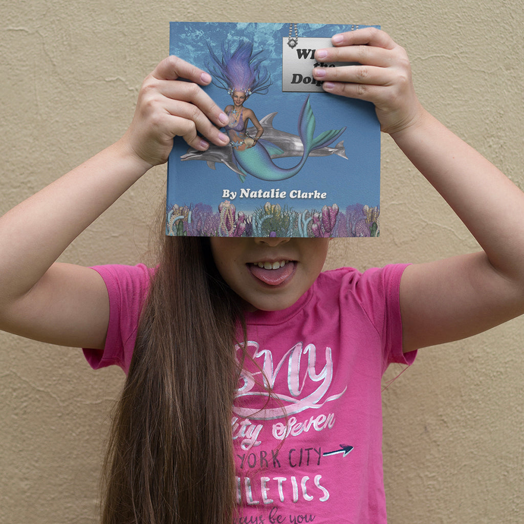 Child holding 'Why Are Dolphins So Smart' book covering face, wearing a pink t-shirt, showing excitement and curiosity.