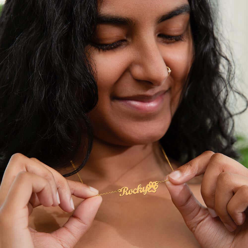 Woman holding personalized More Than Charms Name Paw Necklace, featuring "Rocky" in elegant gold script.